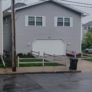 A gray residential house with a garage, viewed from the street on a rainy day.