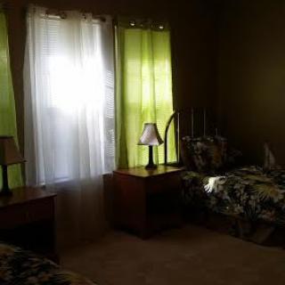 A cozy bedroom with twin beds, nightstands, and green curtains.