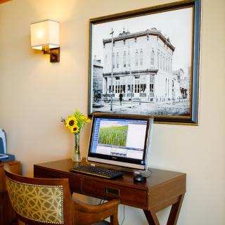 A cozy office setup with a computer on a wooden desk, adorned with flowers and illuminated by a wall lamp.