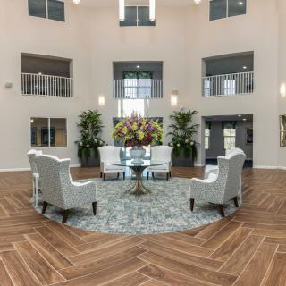A modern lobby with a circular seating area featuring chairs around a table, adorned with plants and natural light.