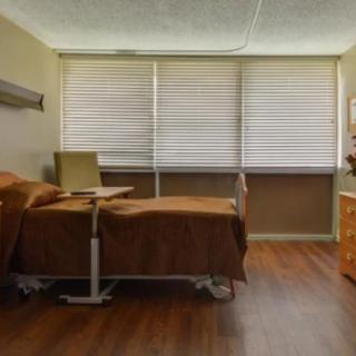 A hospital room with a single bed, chair, and window blinds.
