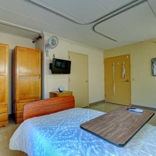 A well-furnished hospital room featuring a bed, wardrobe, and television.