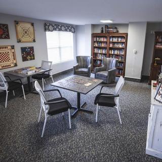 A cozy library room with tables, chairs, and bookshelves filled with books.