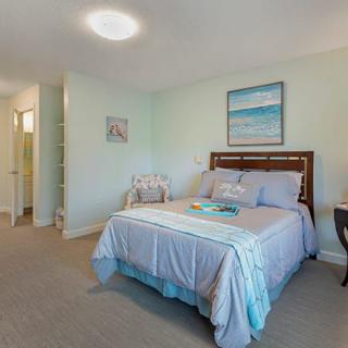 A neatly arranged bedroom with soft, neutral tones and ocean-themed artwork on the wall.