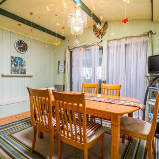 A cozy dining room featuring a wooden table with chairs, illuminated by a chandelier and adorned with colorful ceiling decorations and striped rug.