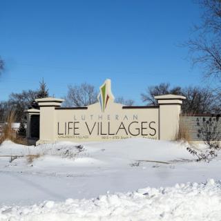 The entrance sign for Life Villages, surrounded by snow in winter.