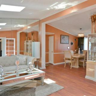A cozy living room with adjoining dining area featuring orange walls and hardwood flooring, illuminated by natural sunlight from the skylight.