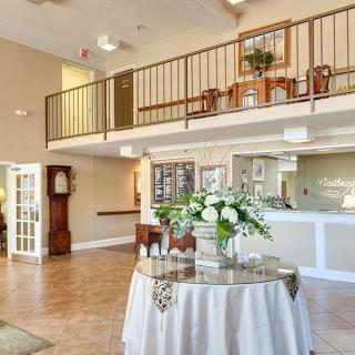 A spacious lobby with a circular table adorned with flowers, a balcony, and various pieces of furniture.