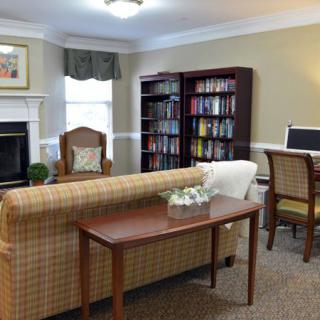 A cozy living room with a sofa, armchair, fireplace, bookshelf, and computer desk.