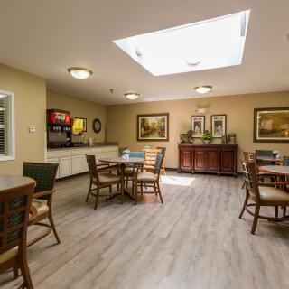 A cozy dining area with several tables and chairs, featuring a skylight and wooden flooring.