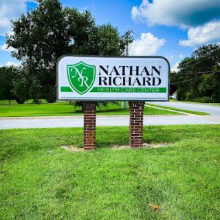 A business sign for Nathan Richard, displayed prominently in a green outdoor setting.