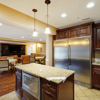 Modern kitchen with granite island and stainless steel refrigerator, leading to a spacious dining area.