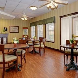 A cozy dining area with wooden floors, tables, and chairs surrounded by large windows.