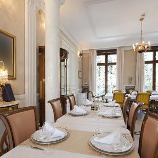 A beautifully set dining room with an elegant classical design, featuring chandeliers and large windows.