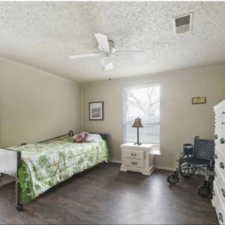 A simple bedroom with a single bed, wheelchair, and ceiling fan.