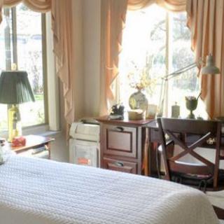 A cozy bedroom interior with a bed, desk, and large windows letting in natural light.