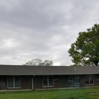 A modest building surrounded by grassy areas and trees under a cloudy sky.