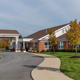 A modern building with a driveway and landscaped surroundings, featuring trees and a well-maintained lawn.