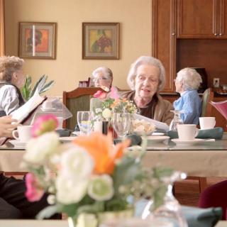 A group of elderly people enjoying a meal together at a beautifully set table with flowers.