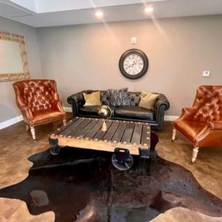 A modern living room with a black sofa, brown leather armchairs, a unique coffee table, and a decorative rug.