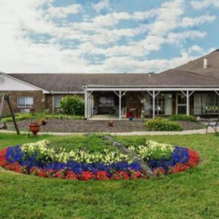 A beautifully maintained garden with colorful flowerbeds in front of a house under a partly cloudy sky.