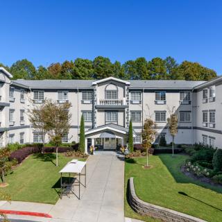 A large residential apartment building with landscaped grounds and a clear blue sky.