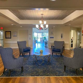 A cozy lobby with a seating area featuring armchairs around a central table, accented by a chandelier and a patterned rug.