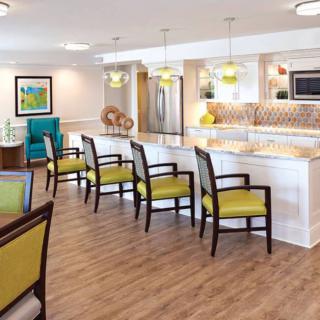A modern kitchen with white countertops, yellow bar stools, and wood flooring.