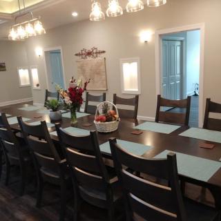 A spacious dining room with a long wooden table set for a gathering, featuring elegant chandeliers and floral decor.