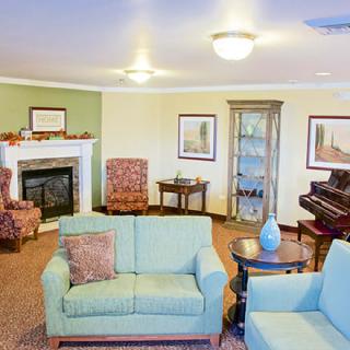 A cozy living room with a fireplace, comfortable seating, and a piano.
