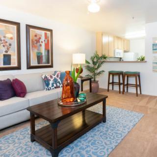 A modern living room with a comfortable sofa, colorful artwork, and a stylish coffee table near the kitchen area.