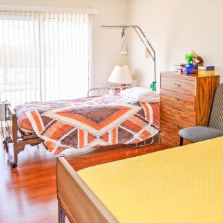 A nursing home room with a hospital bed, bedside table, and lamp.