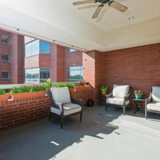 A cozy patio area with comfortable seating, potted plants, and a ceiling fan against a backdrop of brick walls.