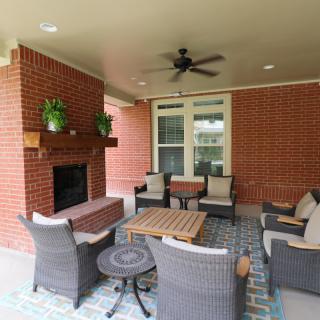 A cozy outdoor patio with rattan furniture, a brick fireplace, and ceiling fan.