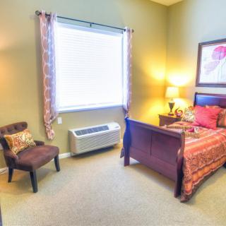 A cozy bedroom with a bed, chair, and lamp by the window.