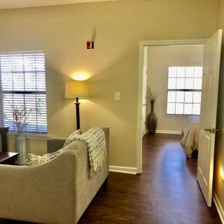 Cozy living room with sofa and lamp leading to a bedroom.