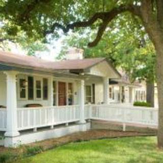 A charming house with a spacious porch and shaded by large trees.