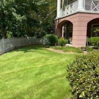 A well-maintained lawn beside a residential building with a white fence.