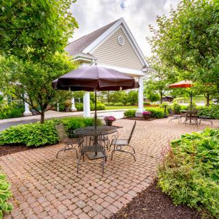 A peaceful garden patio with outdoor seating and umbrellas, surrounded by lush greenery.