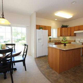 A bright kitchen with a dining area, featuring wooden cabinets and a central island.