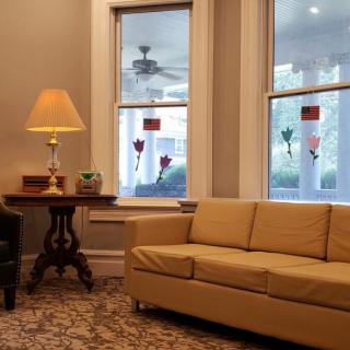A cozy living room featuring a beige sofa, a side table with a lamp, and large windows overlooking a porch.
