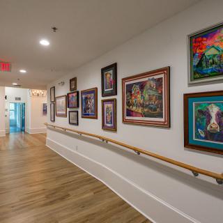 A hallway decorated with a variety of framed paintings on the wall, featuring a wooden floor and soft lighting.