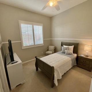 A cozy bedroom featuring a single bed, nightstand with a lamp, and a TV stand opposite the bed.