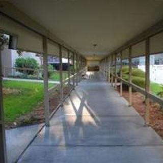 A covered outdoor walkway with railings, leading through a grassy area.