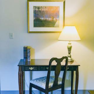 A cozy study nook with a wooden desk, chair, and lamp, complemented by a painting on the wall.
