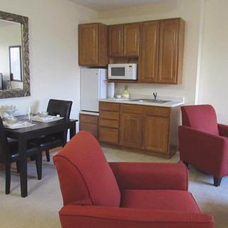 A cozy apartment living area with a kitchenette and red armchairs.