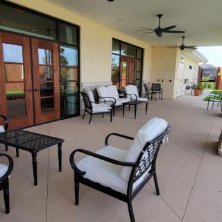 A well-furnished patio with outdoor seating and tables, featuring a covered area and ceiling fan for comfort.