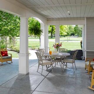 A cozy covered patio with outdoor furniture, overlooking a lush garden.