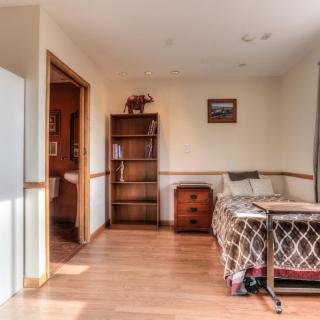 A cozy room featuring a bed, bookshelf, and wooden flooring.