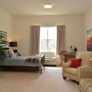 A cozy bedroom with a large window, featuring a bed, armchair, and various decorative elements.